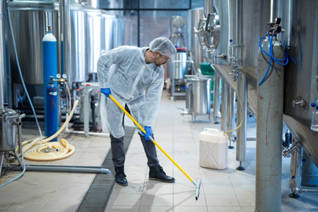 Industrial worker cleaning factory floor near food processing plant