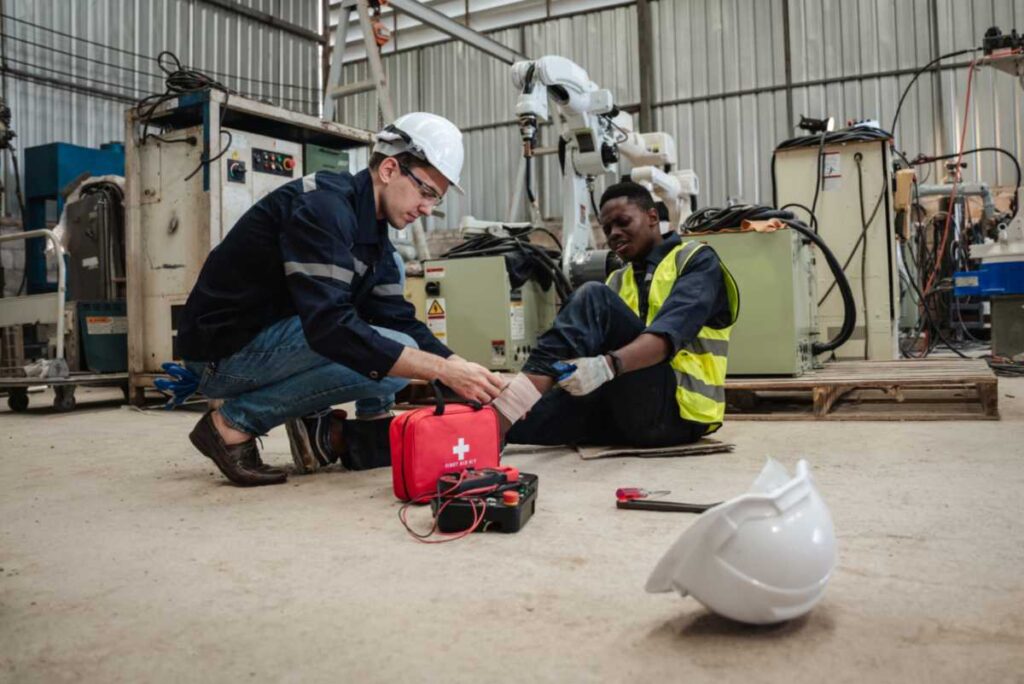 Worker administering first aid to an injured colleague in an industrial workshop